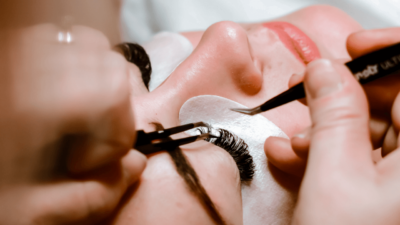 A lash technician with eyelash extension insurance applying lash extensions to a client. 