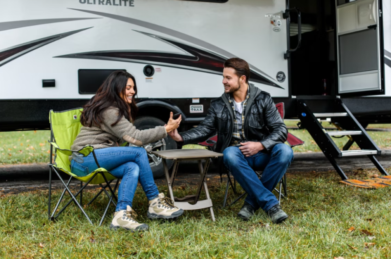Two people sitting on camping chairs outside of an RV. 