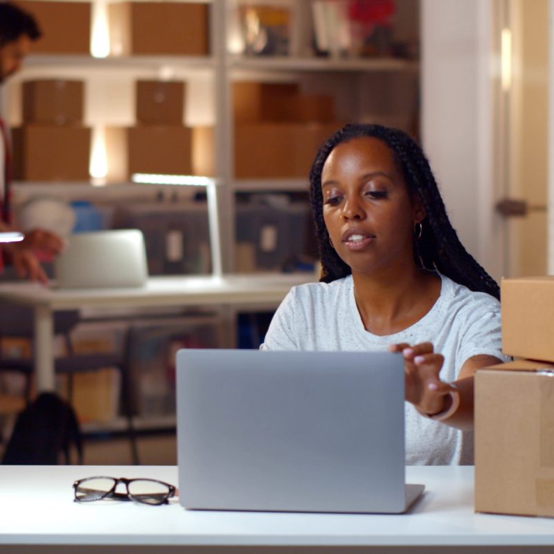 Diverse storehouse managers work in office in evening. African woman and indian man working together in online store warehouse and distribution center