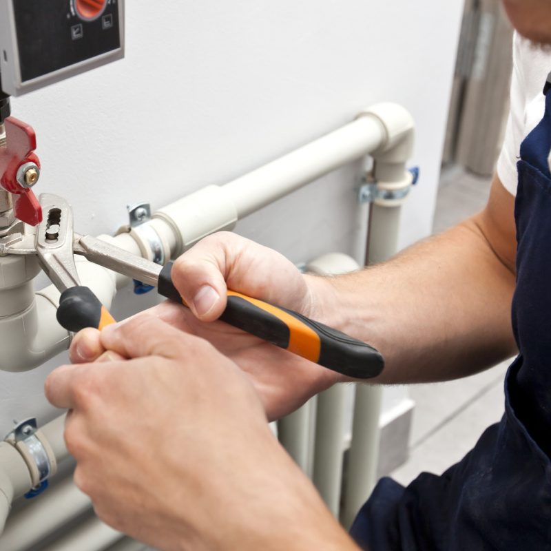 The man is installing the heater system in the house and checking pipes by the wrench