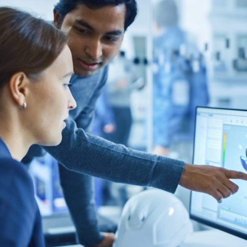 Modern Factory Office: Portrait of Male Project Supervisor Talking with a Female Industrial Engineer, They Point at Computer Display Showing CAD Software with 3D Engine Concept. Team Problem Solving